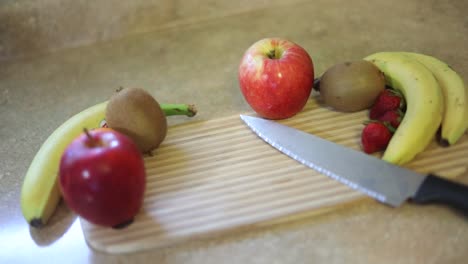 Tiro-A-Cámara-Lenta-De-Una-Variedad-De-Frutas-En-Una-Tabla-De-Cortar-Con-Un-Cuchillo-Junto-A-Ellos