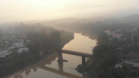 Side-panning-shot-of-old-bridge-over-mekong-river-Luang-prabang,-aerial