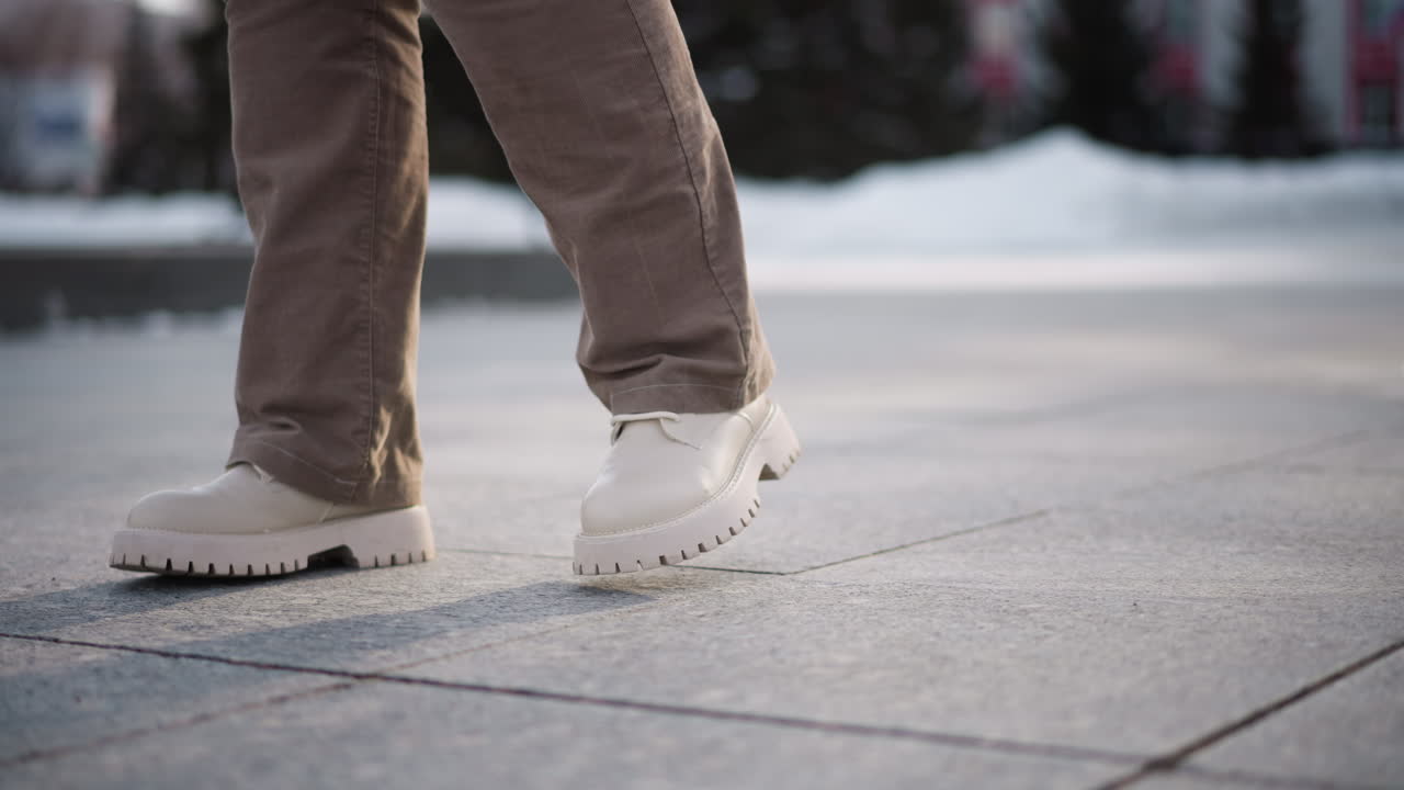 Leg view of young lady dancing on tiled outdoor floor wearing corduroy trousers and canvas boots capturing rhythmic motion against urban pavement with winter light and snow backdrop