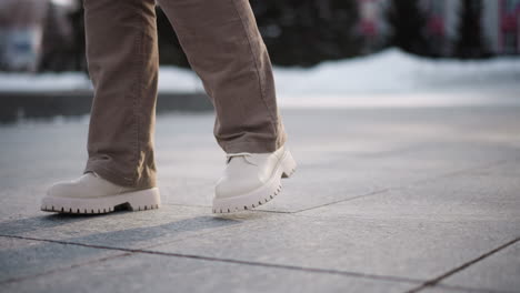 leg view of young lady dancing on tiled outdoor floor wearing corduroy trousers and canvas boots capturing rhythmic motion against urban pavement with winter light and snow backdrop