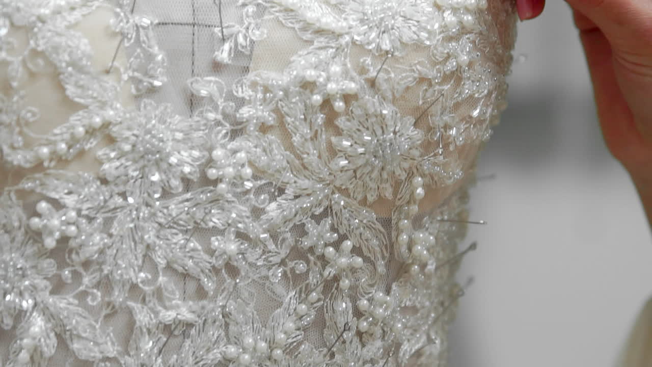 Primo piano di una stilista per spose nel suo studio, con spilli e aghi su un abito da sposa in pizzo. La sarta crea un abito da sposa esclusivo. Fissa i contorni con spilli e aghi. Piccola attività privata.