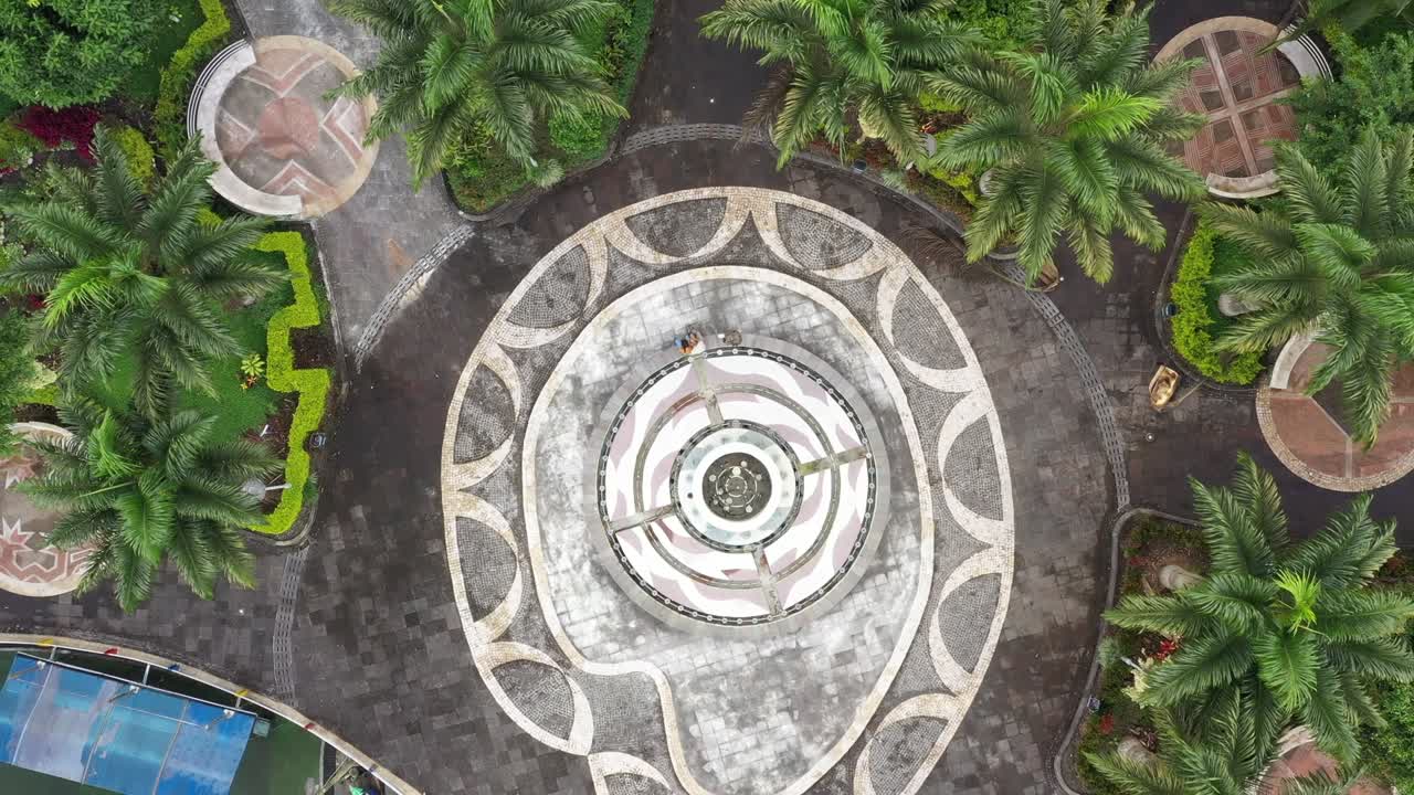 많은 선의 패턴을 보여주는 모자이크가 있고 큰 종려나무로 둘러싸인 작은 공원의 분수에서 확대