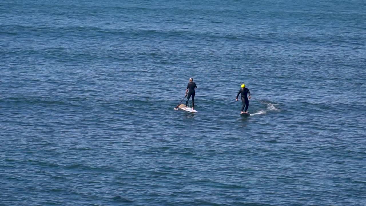 Surfer assisted by Foil Drive heading towards the outside, gliding smoothly over the ocean's surface in the middle of SUP paddles, with the motor aiding in the momentum