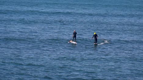 surfer assisted by foil drive heading towards the outside, gliding smoothly over the ocean's surface in the middle of sup paddles, with the motor aiding in the momentum