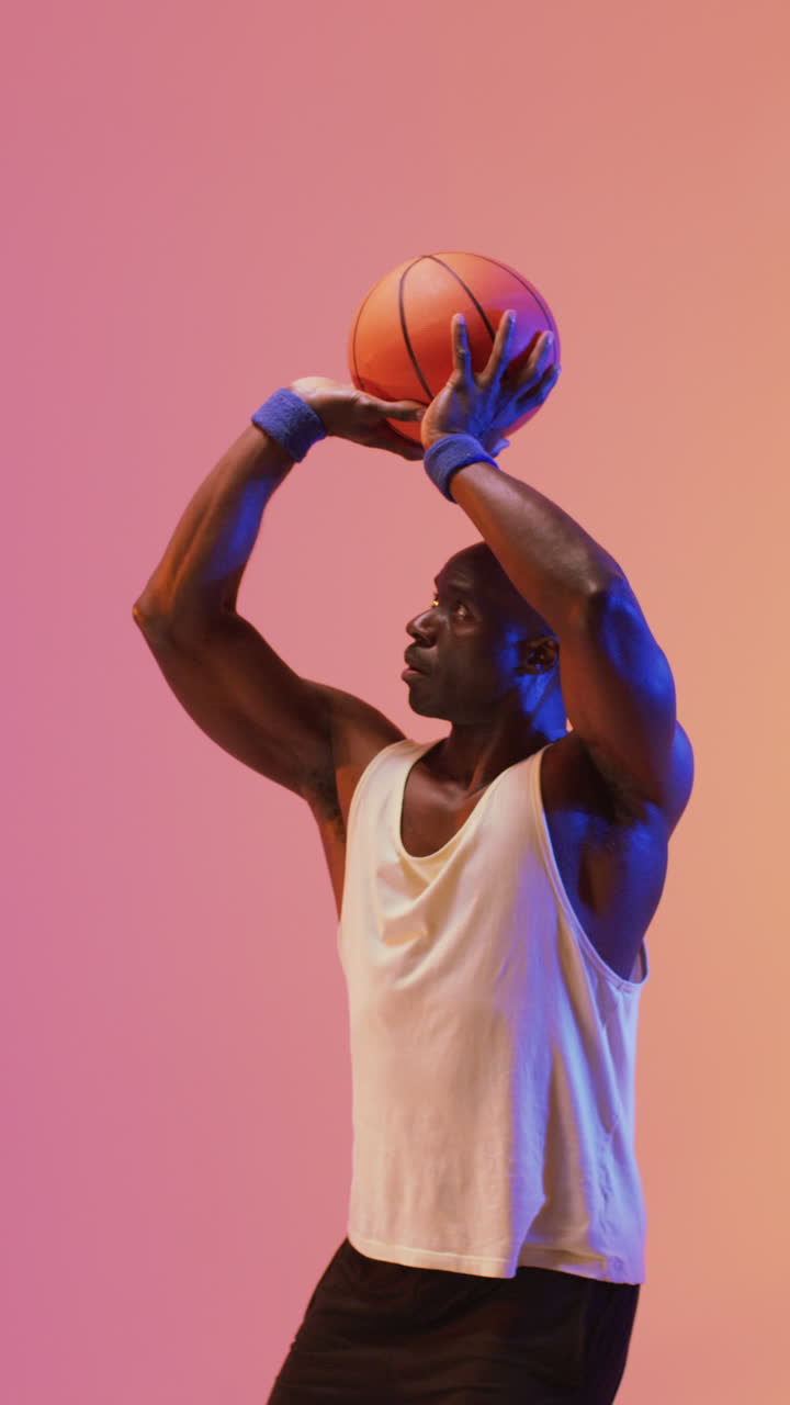 video vertical de un jugador de baloncesto afroamericano lanzando una pelota sobre un fondo rosa