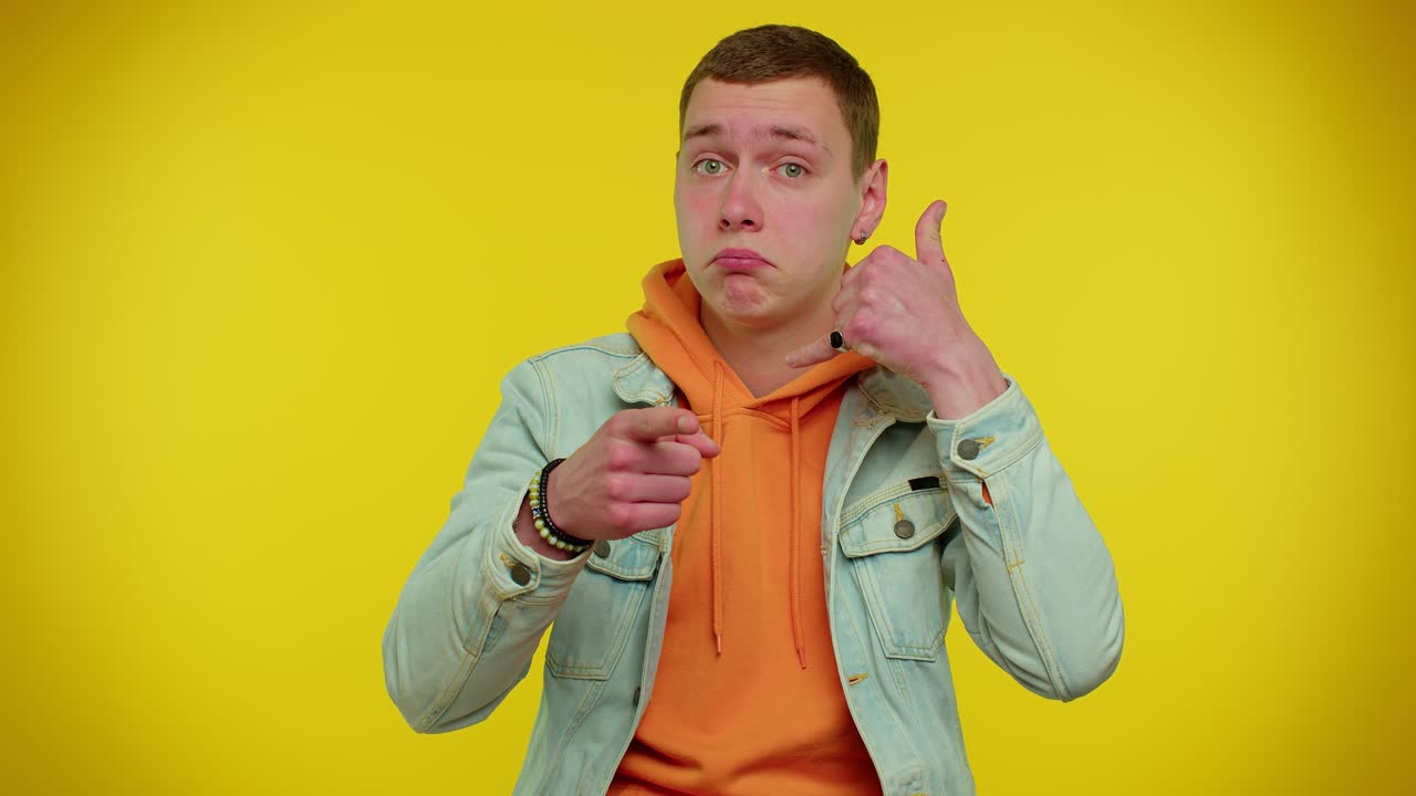 청바지 재을 입은 쾌활한 남자가 카메라를 바라보며 전화 제스처를 하고 있습니다.