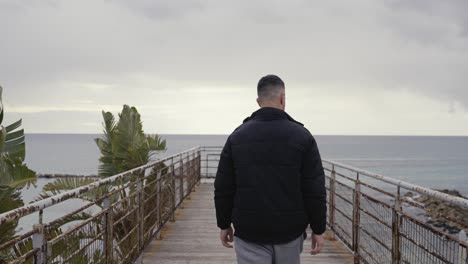 slow motion tracking shot, following a man walking down a pier towards the sea