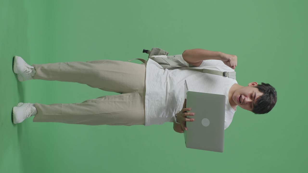 cuerpo lleno de estudiante hombre asiático usando computadora portátil y celebrando en pantalla verde estudio