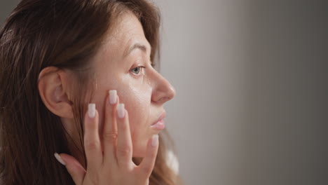 woman applies cream to area of face under eyes. attractive woman carefully monitors skin on face treating with special cosmetics slow motion