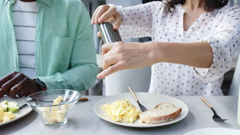 happy biracial couple seasoning and having scrambled eggs for breakfast in kitchen, slow motion