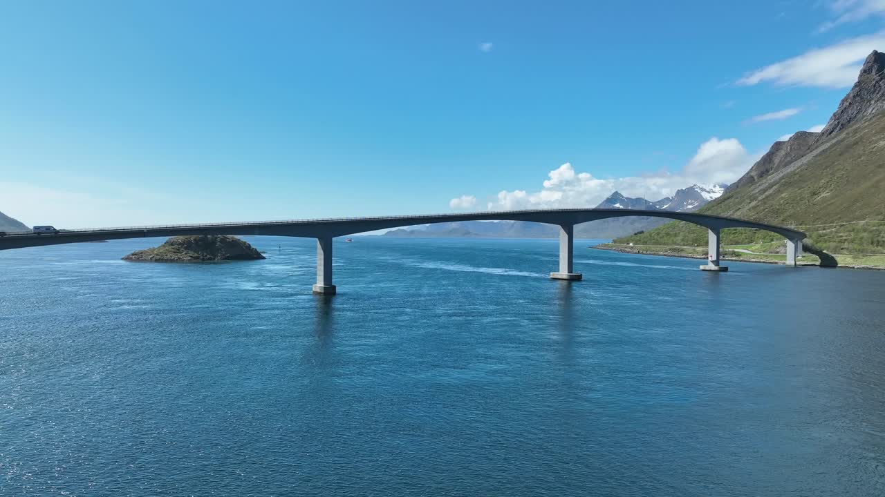 Aerial of a car crossing Bridge to Gimsoy, Lofoten, Norway along scenic E10 Highway, flying left to right