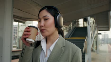 woman drinking coffee at train station while listening to music