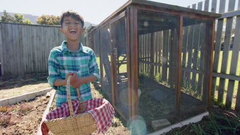 portrait of happy biracial boy holding basket with eggs next to henhouse, slow motion, copy space