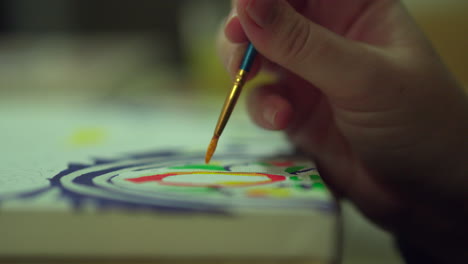 Close-up-of-female-hand-holding-paint-brush-whilst-painting-a-colourful-canvas