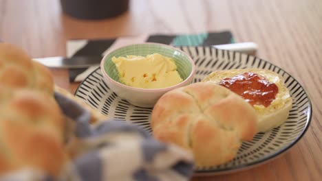 Kaiser-Bread-with-Butter-and-Jam-on-the-Plate-on-Wooden-Table,-Close-Up