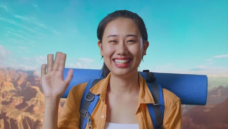 close up of asian female hiker with mountaineering backpack waving hand and saying bye while traveling at the top of mountain