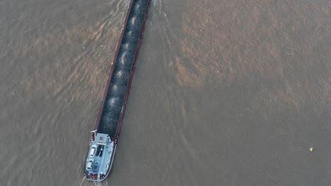 Loaded-cargo-ship-driving-ahead-in-muddy-water-in-Rhine-river.-Tilt-up-reveal-of-bridge-and-buildings-on-banks.-Cologne,-Germany