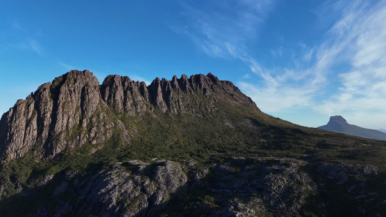 Aerial backwards of Cradle Mountain Peak against blue sky in summer. Steep famous rocky mountainside in summer. Tasmania, Australia. Wide shot