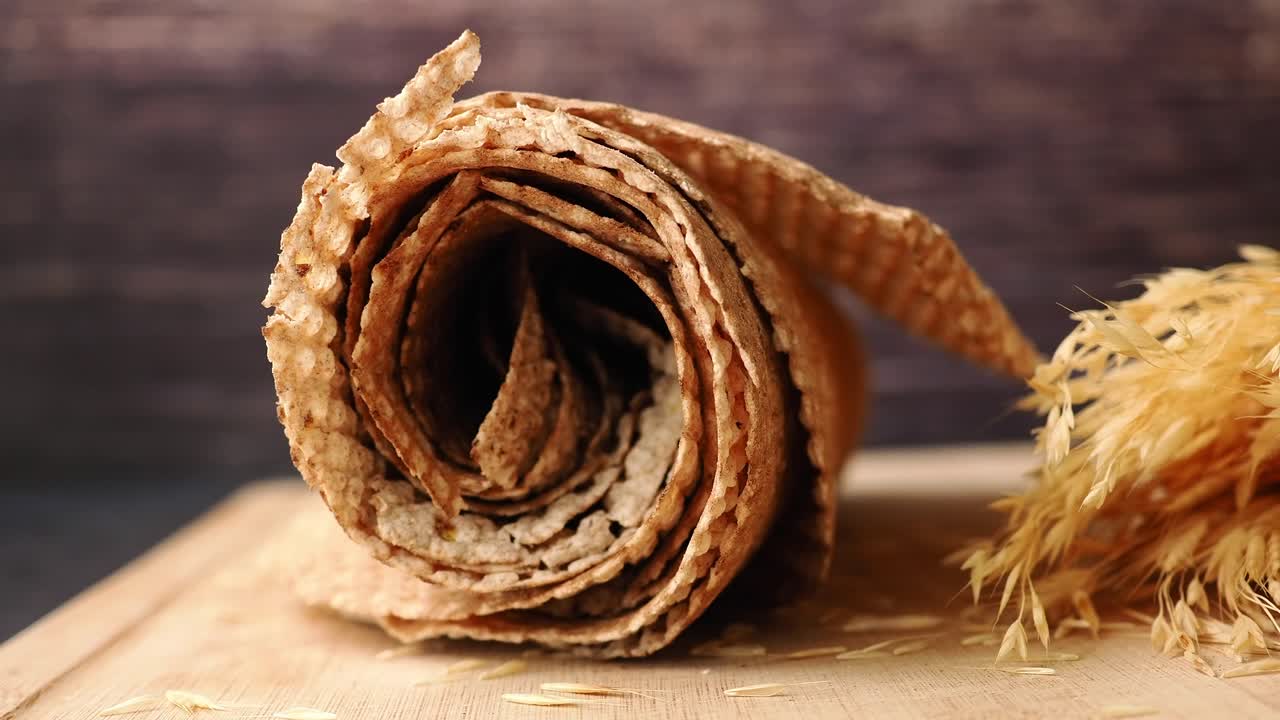 Pane piatto arrotolato e spighe di grano su un tagliere di legno