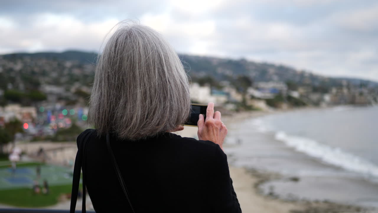Una donna anziana in vacanza che scatta una foto con il suo telefono della città e dell'oceano a Laguna Beach, California SLOW MOTION