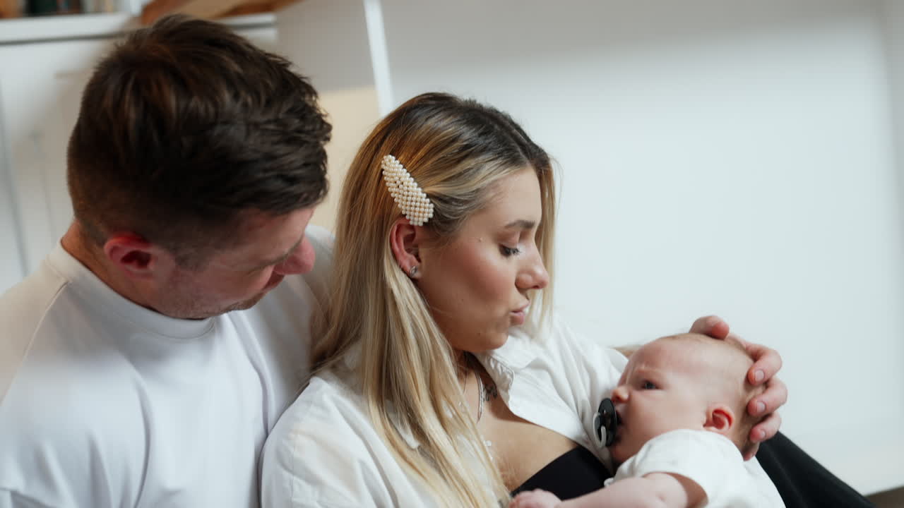 Caucasian family of three. Parents sit together looking at their newborn baby boy. Close up.