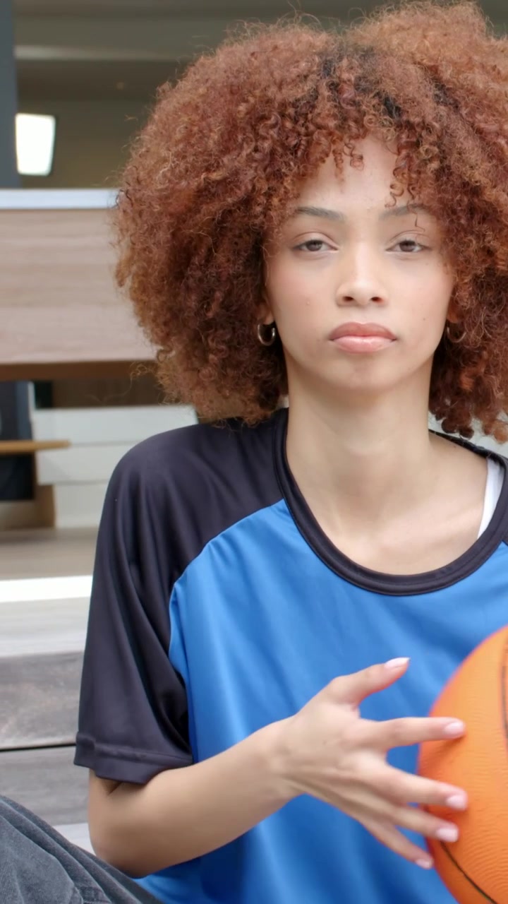 Vídeo vertical: Reagindo ao close-up, mulher de blusa azul rolando bola laranja nos degraus para praticar.