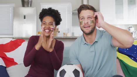 video de una feliz pareja diversa con banderas de portugal e inglaterra y viendo el partido en la televisión