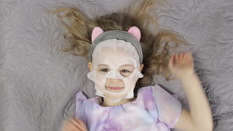 Teen-girl-with-moisturizing-face-mask.-Child-kid-take-care-of-skin-with-cosmetic-facial-mask