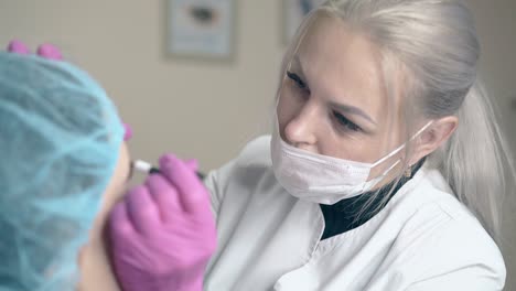 master in mask makes brows tattooing on woman face in clinic