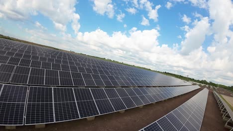 Vista-Aérea-De-Drones-Fpv-Volando-Bajo-Sobre-Una-Matriz-De-Paneles-Solares-Fotovoltaicos-Bajo-Un-Cielo-Azul-Nublado