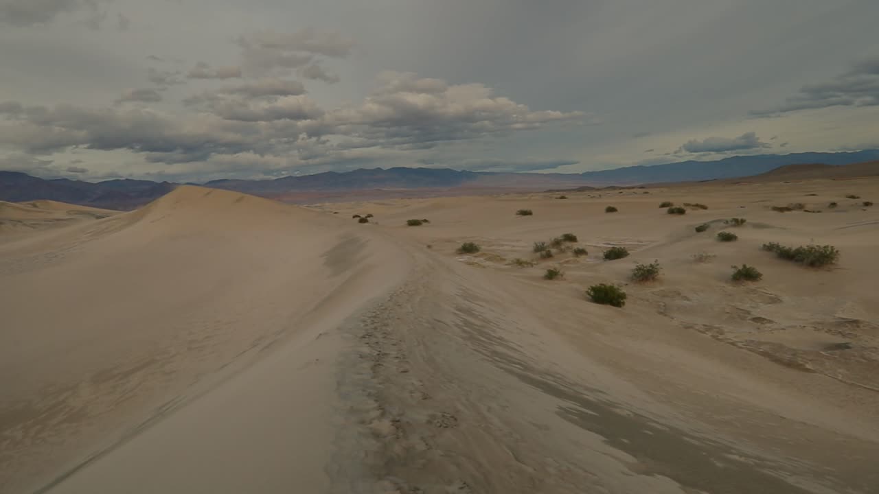 젖은 모래 언덕을 오른쪽에서 왼쪽으로 천천히 이동하고 수평선에 파스텔 산이 보입니다.