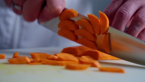 a chef cutting a carrot on a cutting board with a knife