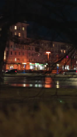 close view of an urban street at night with illuminated buildings and street lights, with car passing on the road