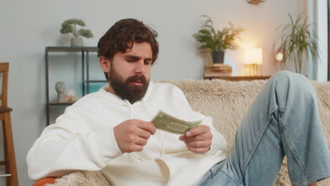portrait of poor arabian man upset over insufficient amount of money showing one dollar banknote