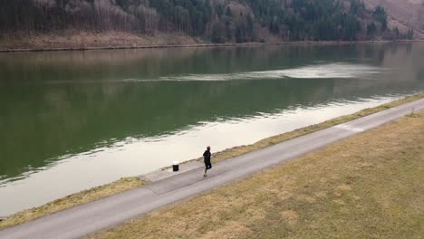 drone footage of a man walking next to a river pans to the right