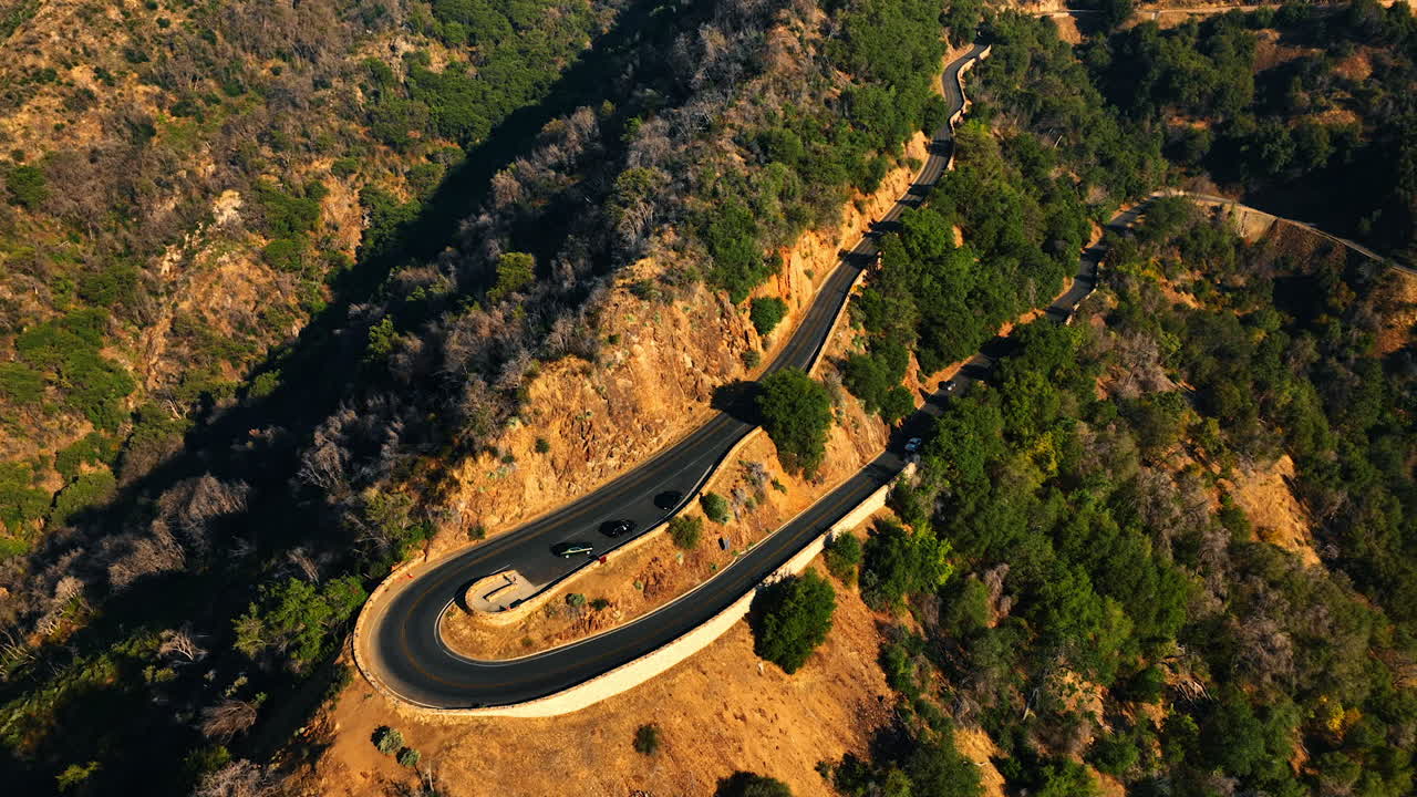 Highway turn on the mountain top. Some cars stand on the road near the slope. Drone footage on sunny day.