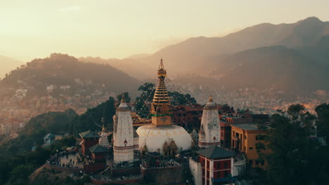 the drone abruptly reveals the magnificent swayambhunath stupa in kathmandu, nepal, also known as monkey temple, against the backdrop of lush green hills and a golden evening sky.