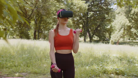 Athletic-girl-in-VR-headset-helmet-making-fitness-workout-exercises-with-dumbbells-outdoors-in-park