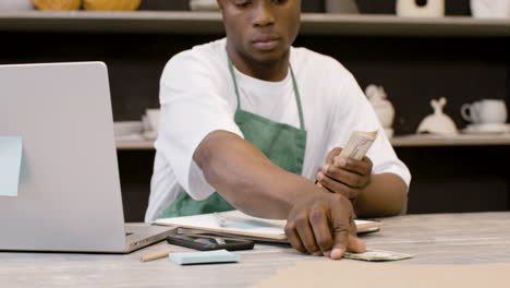 male small business owner counting money and using phone calculator in the pottery shop