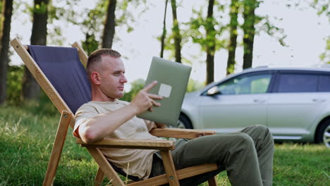 caucasian man working remote in nature is feeling tired. man takes a break covering his face with laptop.