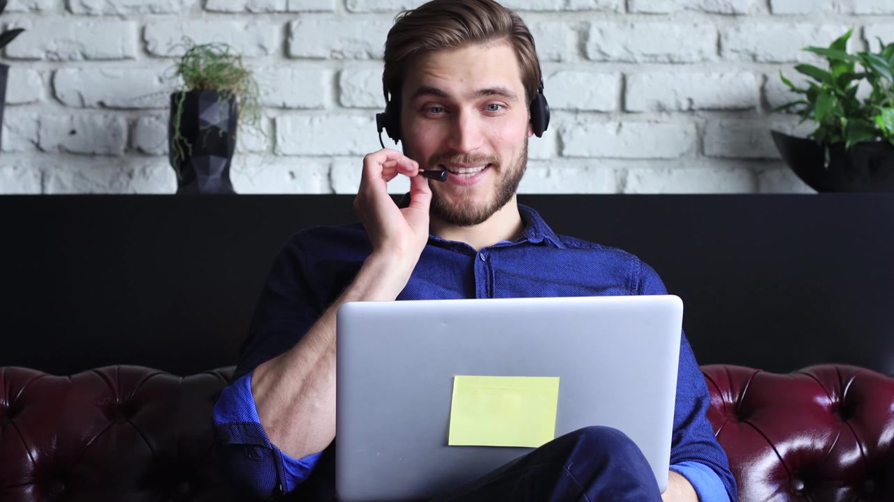 Smilende mand i headset taler i videoopkald med bærbar computer