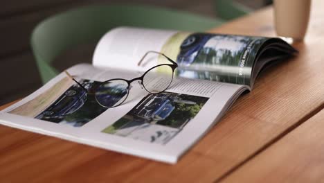 open magazine with glasses on wooden table