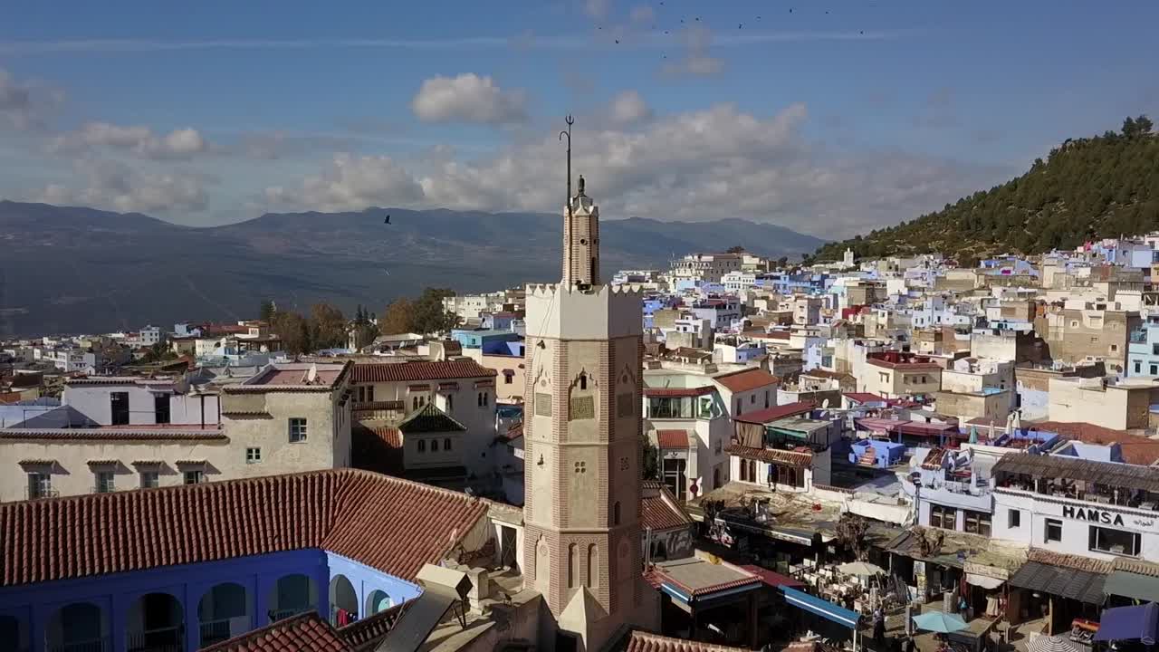 Vista aerea ravvicinata del minareto di una moschea a Chefchaouen, Marocco, che domina la medina della città blu e il paesaggio dei Monti del Rif alla luce del giorno.