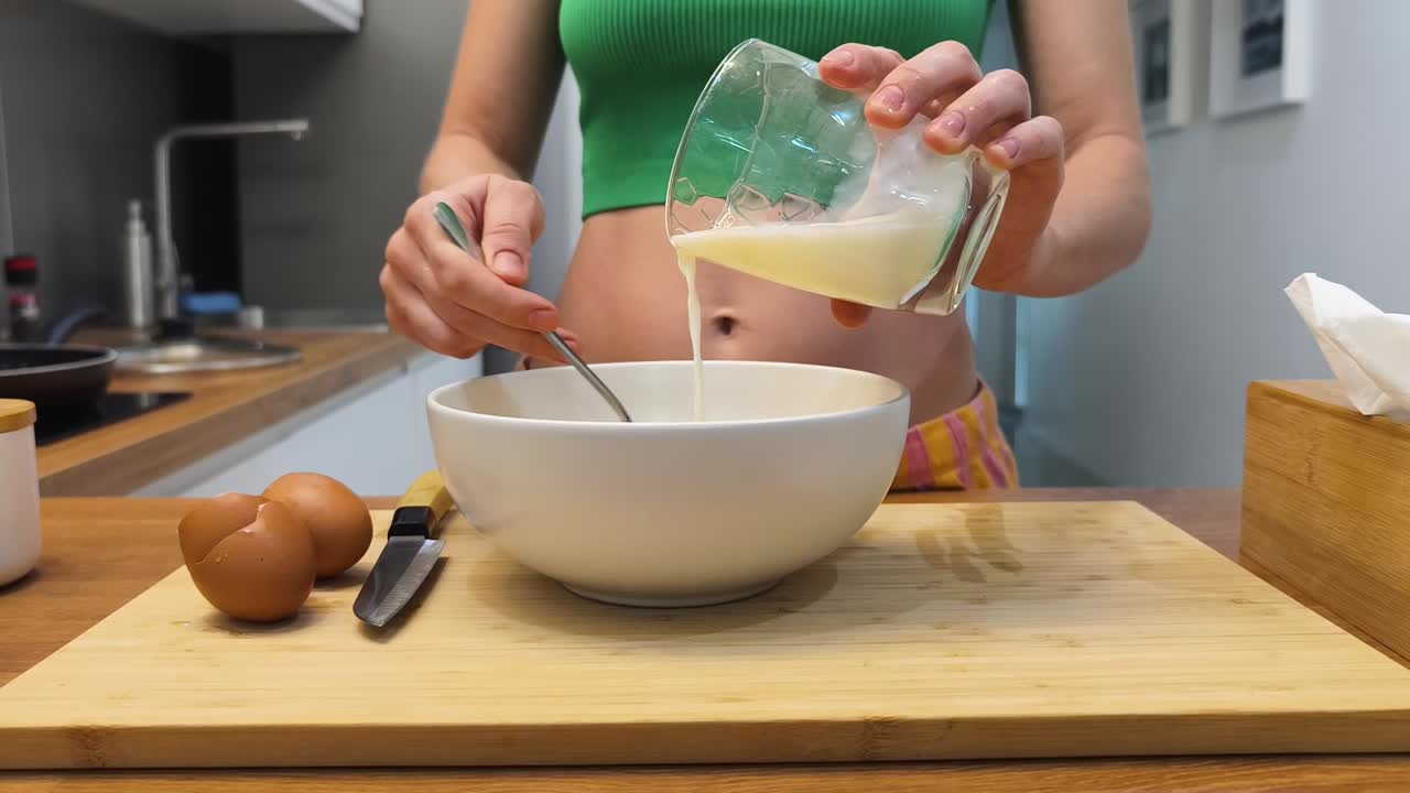mujer vertiendo leche en un tazón con huevos