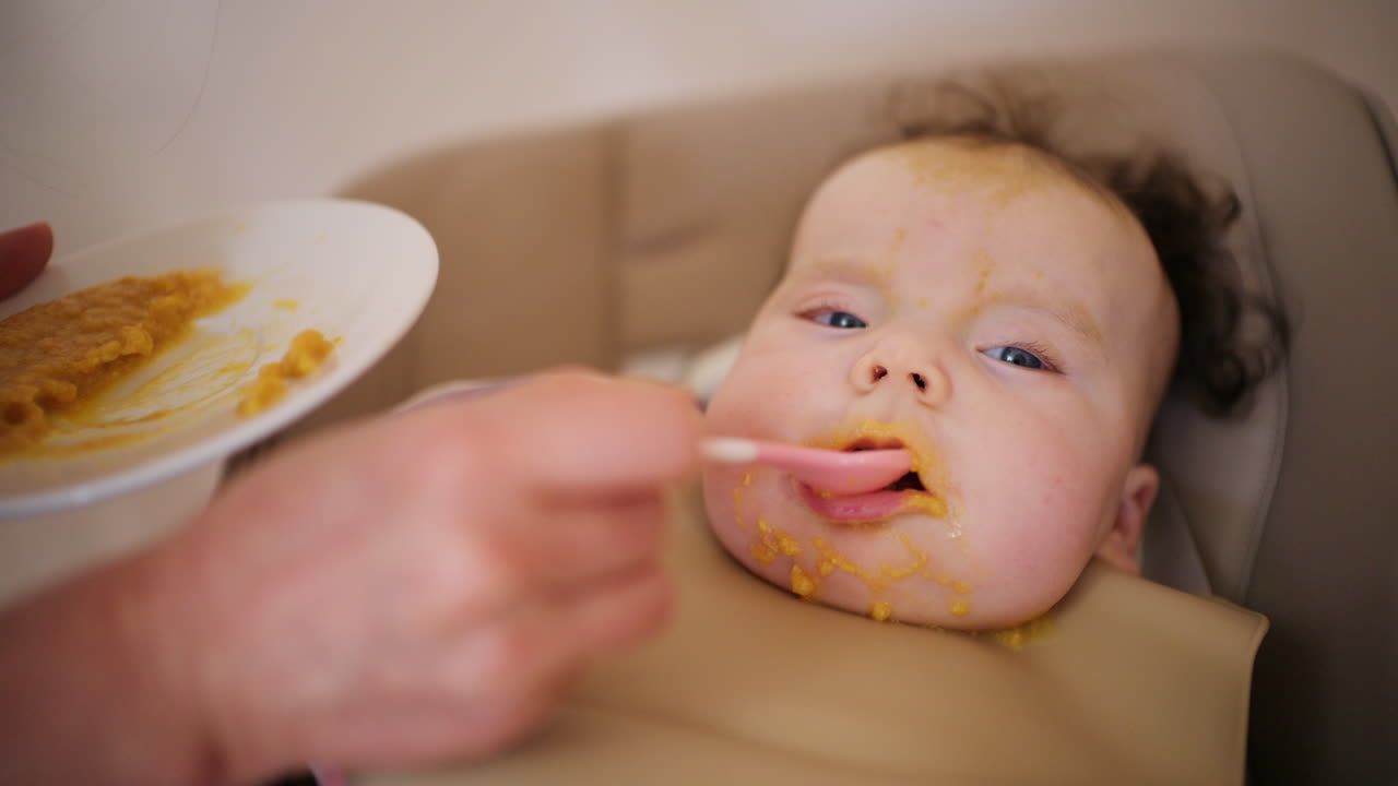 ハイチェアに座る赤ちゃんに大人がスプーンで離乳食を与えている。