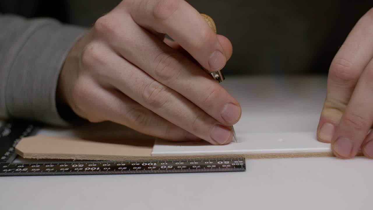 A leatherworker carefully uses an awl to mark stitching holes on a leather strap, ensuring precision in handmade leathercraft.