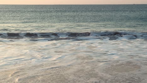 the cinematic moment of the beach near the sea, with waves gently splashing the shore during the evening, unveils the expanse of the ocean surface