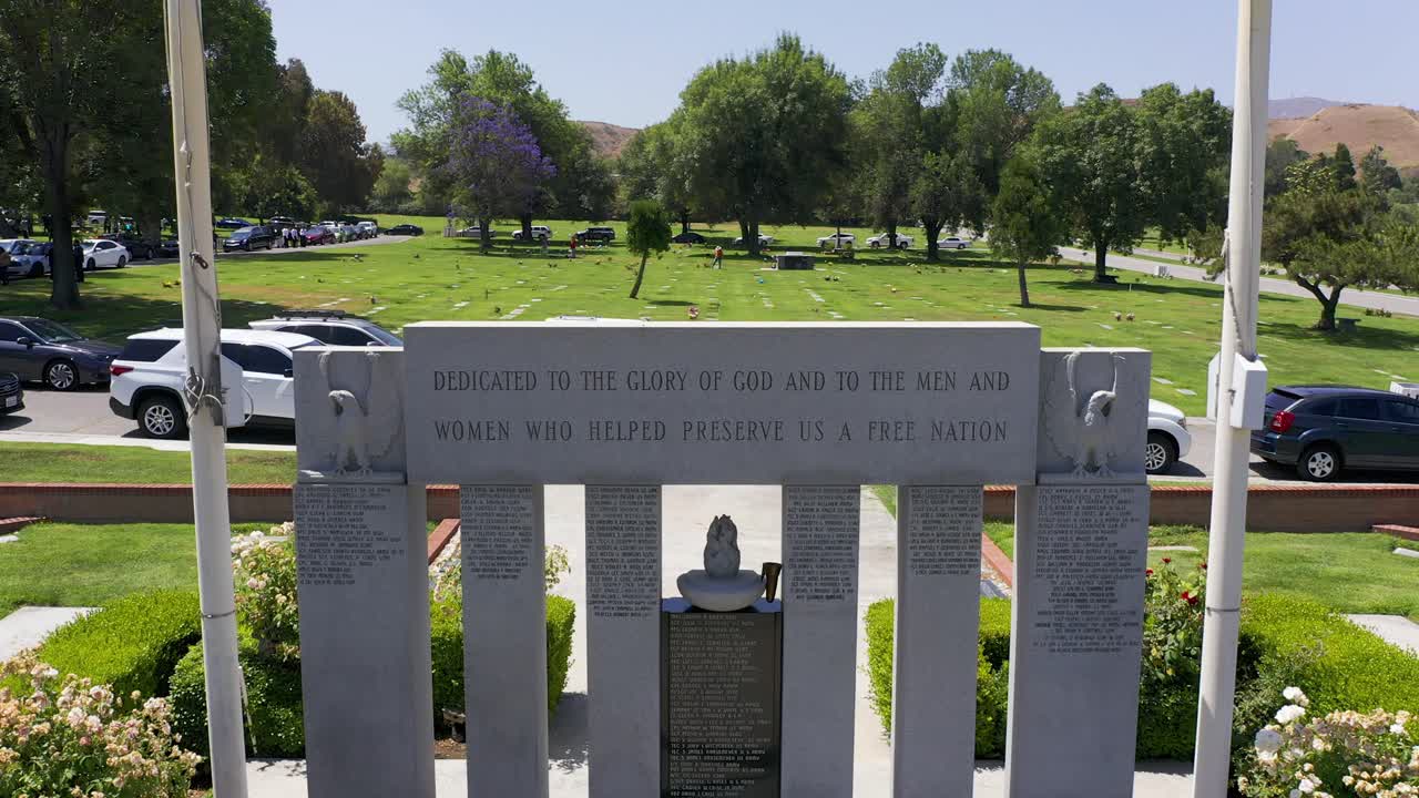 Rising close-up aerial shot of the United States and California flags above a Veteran's War Memorial at a California mortuary