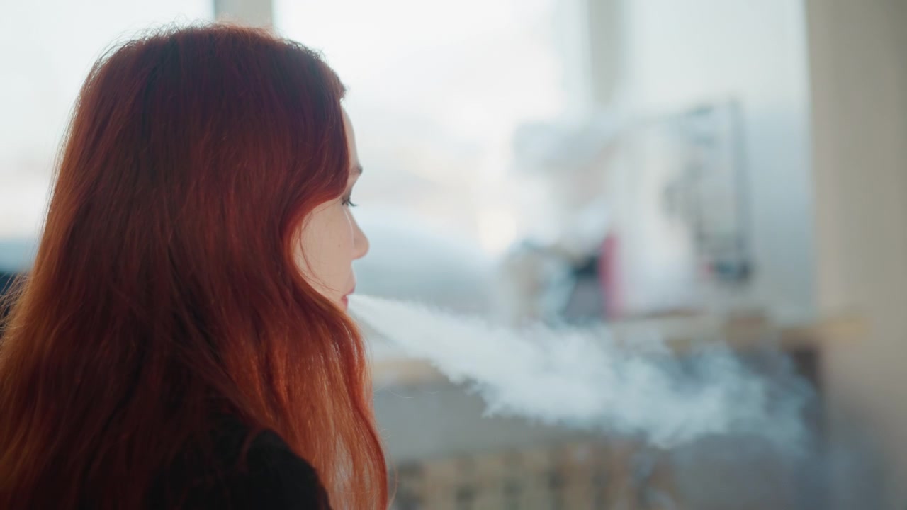 Profilo di una donna dai capelli rossi che esala fumo mentre guarda fuori dalla finestra, luce diurna soffusa e bokeh sullo sfondo, un interno domestico tranquillo evoca un'atmosfera pensierosa e solitudine, con un sottile termosifone vintage e un arredamento accogliente a fare da cornice.