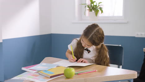 chica concentrada escribiendo en un cuaderno durante la clase de inglés en la escuela mientras el profesor se acerca y revisa su trabajo